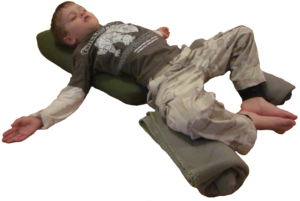 Young boy practicing yoga nidra lying with prop supports.